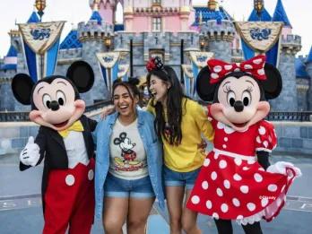 Two friends laughing while posing with Mickey Mouse and Minnie Mouse in front of Sleeping Beauty Castle
