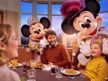 Mickey Mouse and Minnie Mouse in royal attire greeting a family dining at the Royal Banquet inside Disneyland Hotel in Disneyland Paris