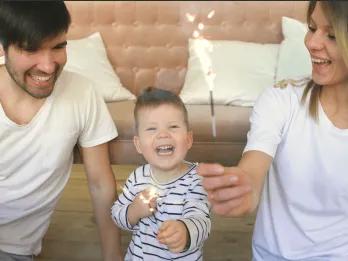 A young family celebrating together at home with sparklers, smiling and laughing