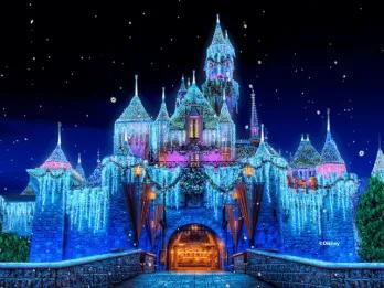 Sleeping Beauty Castle at Disneyland Resort glowing at night with shimmering icicle lights, holiday wreaths, snow-capped turrets, and falling snow effect