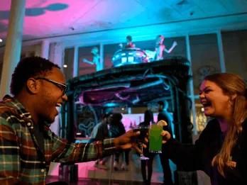 Two guests laughing and clinking colorful themed cocktails at a Universal Orlando Resort hotel Halloween Horror Nights bar experience