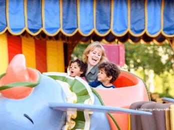 A smiling woman and two young boys riding the Dumbo the Flying Elephant attraction