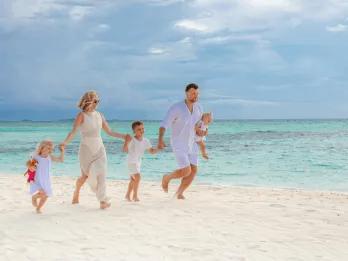A family dressed in white holding hands and running along a tropical white-sand beach