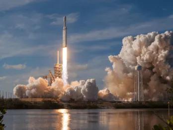A SpaceX Falcon Heavy rocket launching from the pad, surrounded by large plumes of exhaust