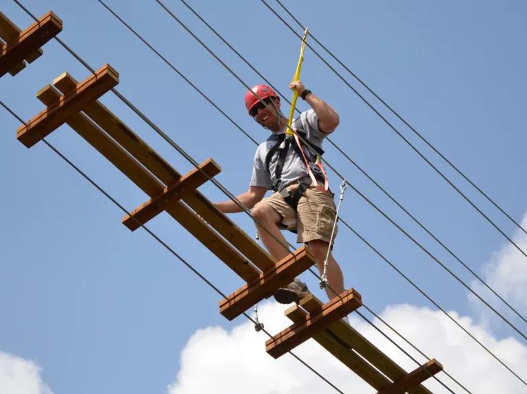 Man traversing swinging bridge on the Sceamin Gator Zip Line course at Gatorland in Florida