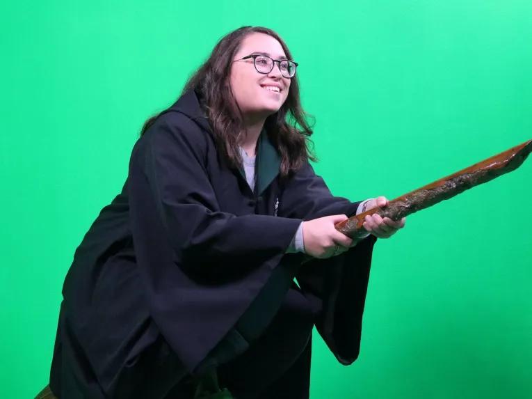 Girl riding a broom in front of a green screen at the Warner Bros. Studio Tour London
