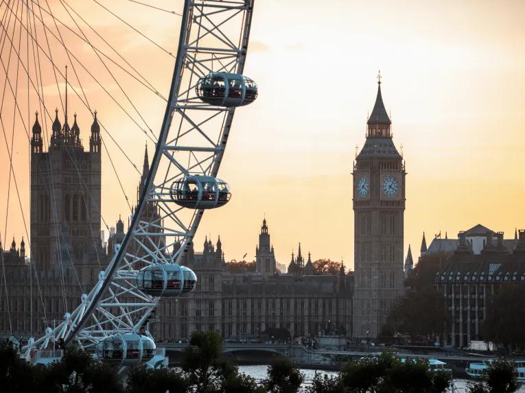 The London eye, a circular ferris wheel with large glass pods on, in front of a large ancient building and clock tower known as the Houses of Parliament and Big Ben.