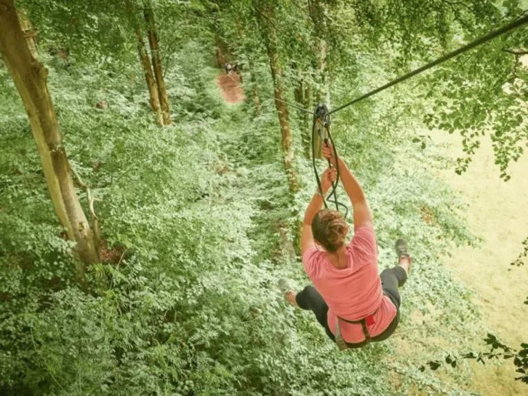 Woman in tree tops zooming down steep zip line that connects to the floor. 