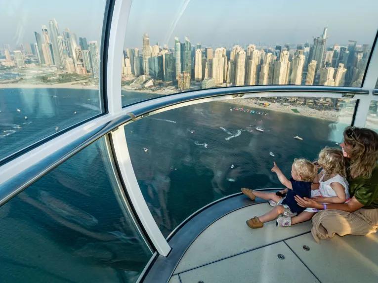 A mother and two young children enjoying the panoramic views of Dubai from a capsule on Ain Dubai.