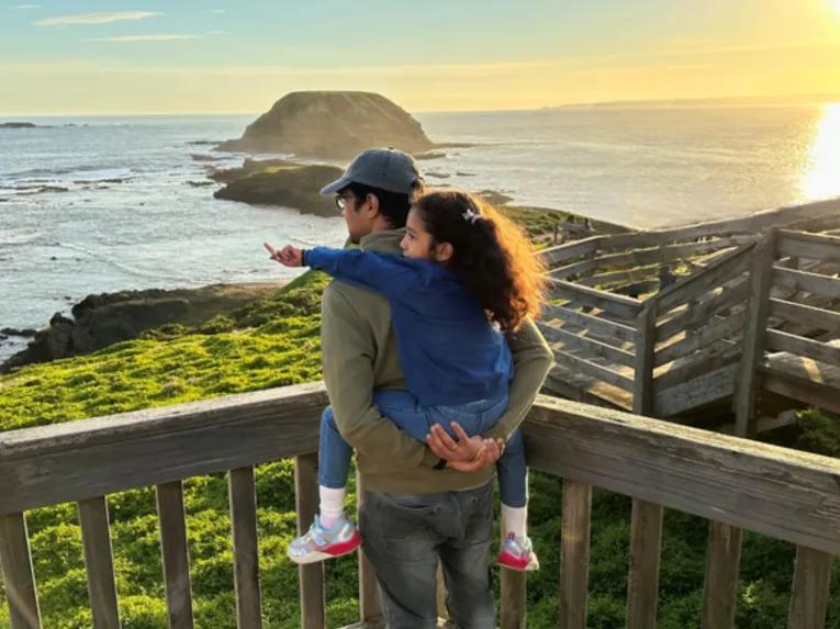 Father carrying child on his back while watching the sunset over the Nobbies coastline
