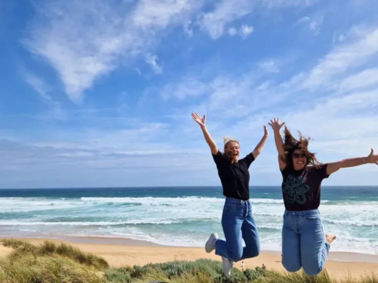 Two women jumping with arms raised at Cape Woolamai with the beautiful ocean in the background