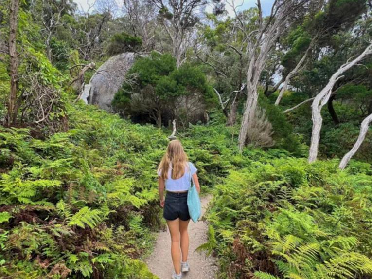 Woman walking toward Tidal River surrounded by natural bushland at Wilsons Promontory
