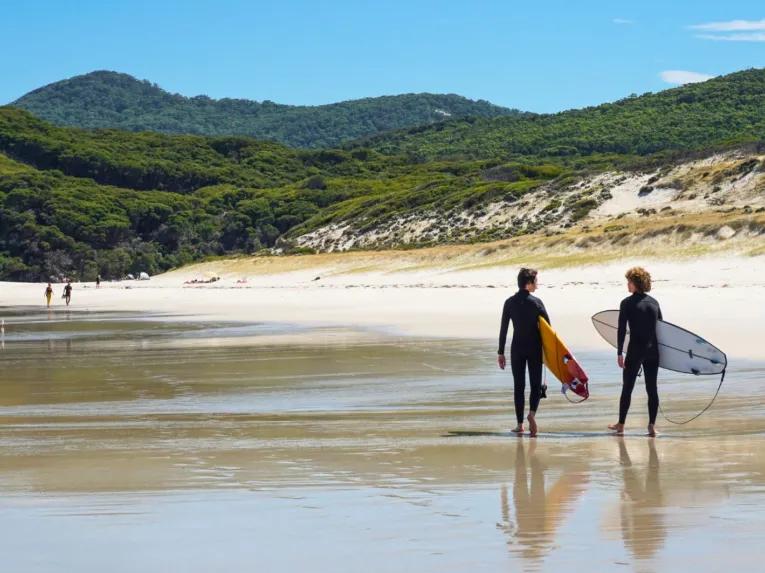 People walking with surfboards along the white sands of Squeaky Beach at Wilsons Promontory