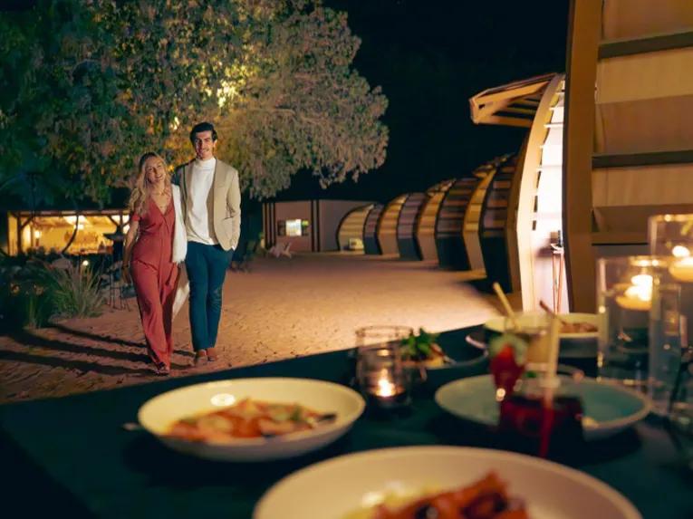 ouple walking toward a candlelit dinner setup at a luxury desert camp