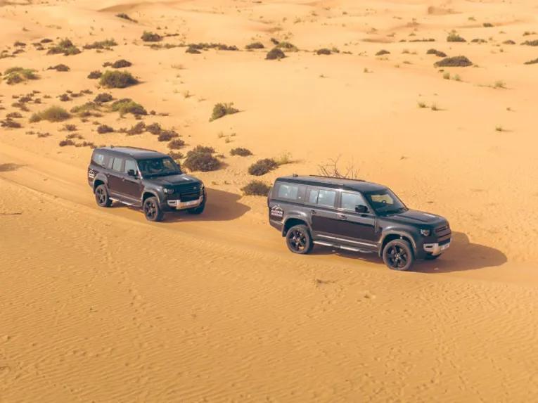 Two Land Rover Defenders driving through the Dubai desert