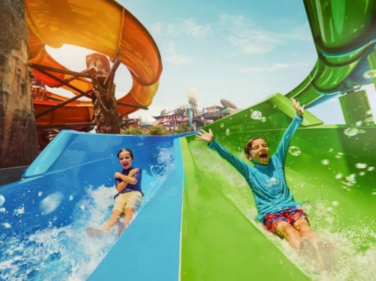 wo children smiling as they go down a water slide at Yas Waterworld Abu Dhabi