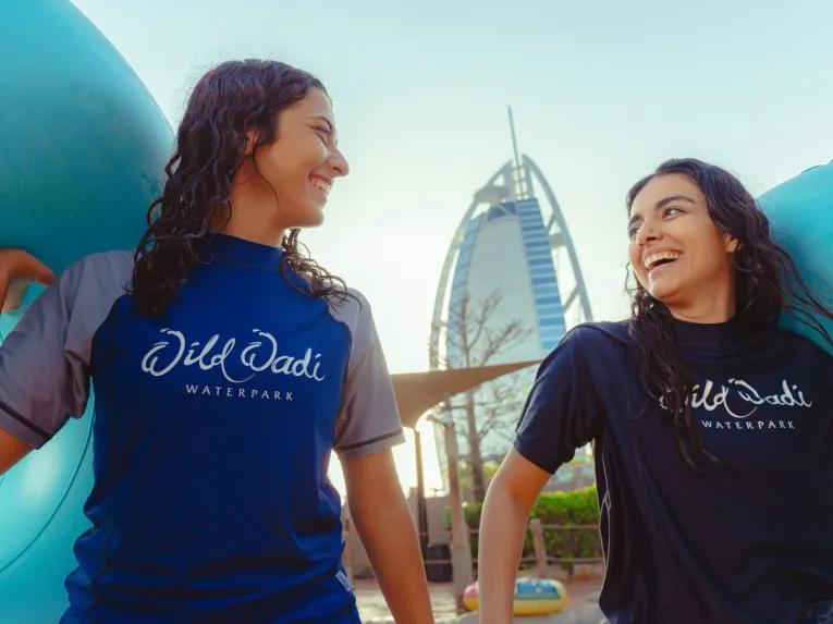 Two women smiling, ready for a water ride at Wild Wadi Waterpark with Burj Al Arab in the background