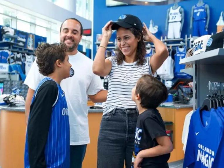 A happy family trying on team hats and browsing apparel inside the Orlando Magic team store.