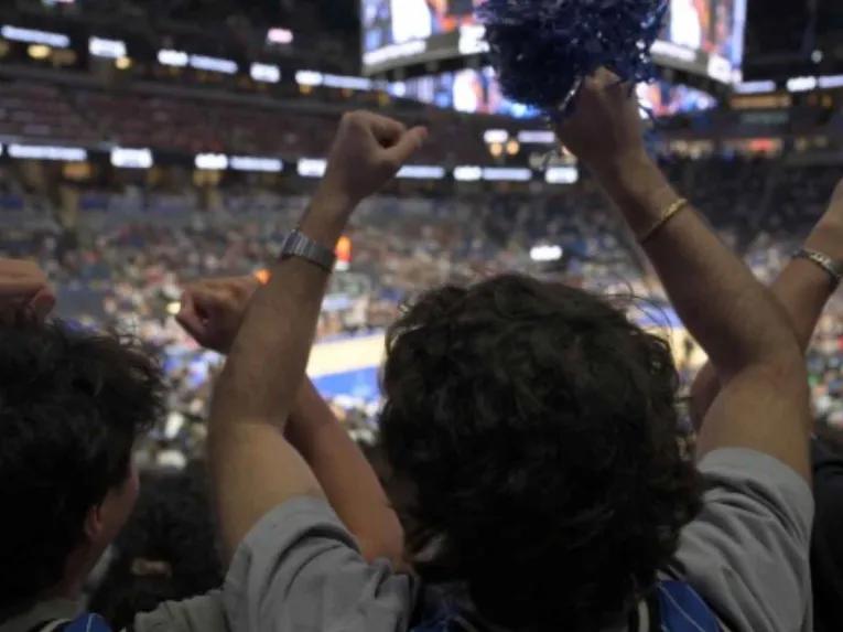 Orlando Magic fans in team jerseys cheering with raised fists and pom-poms