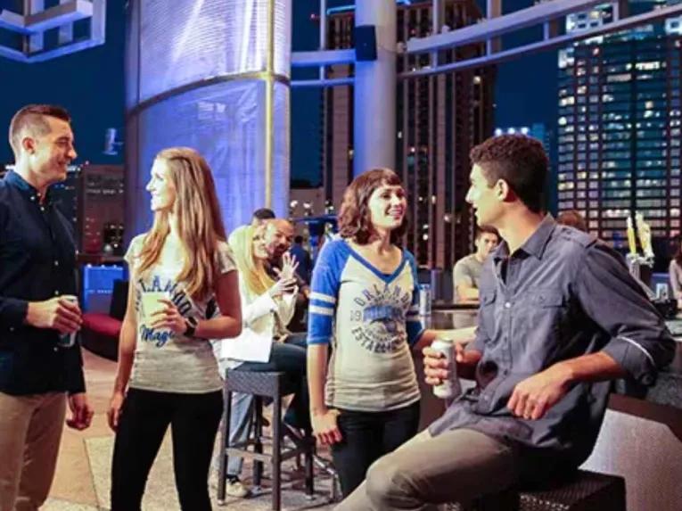 Friends enjoying drinks at a rooftop lounge at Kia Center with downtown Orlando behind them