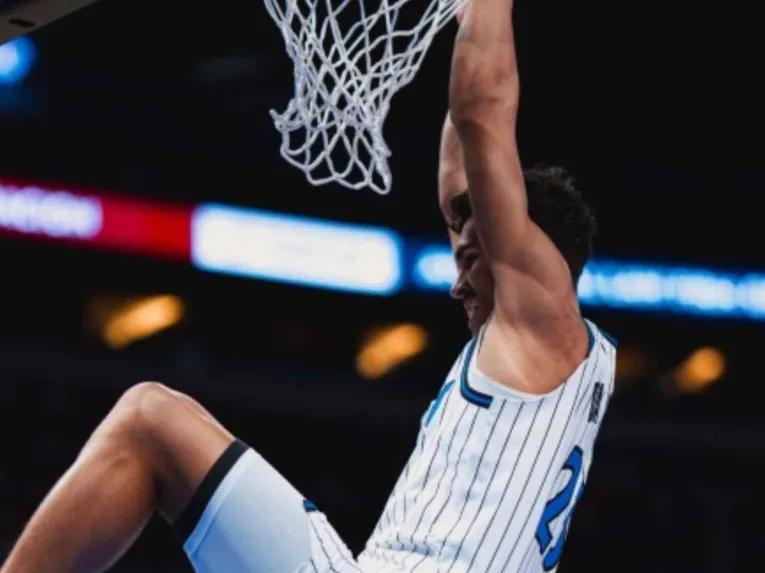 Franz Wagner hanging on the basketball rim after dunking at an Orlando Magic home game