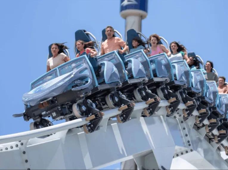 Riders cresting a hill on Penguin Trek roller coaster against a clear blue sky at SeaWorld Orlando